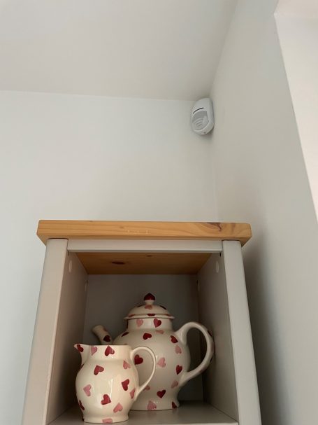 Wireless intruder alarm detector Pyronix KX2 shown mounted in corner of room above a display stand