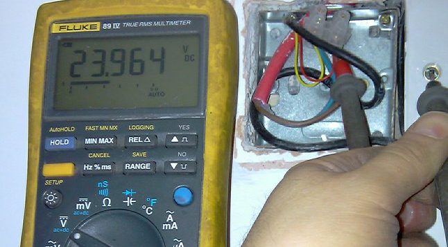 Voltage measurement of fire alarm link connection using a Fluke 89 IV multimeter. Reading shows 23.964V to earth.